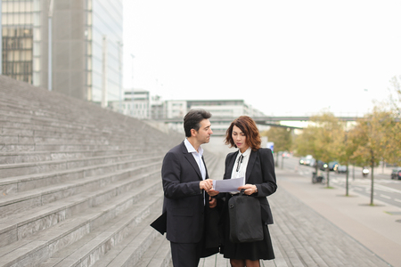 Layer and client standing on big gray stairs. Woman hold documents about court statement in hand. Man tell about very good end of litigation, and bouth smiling look really happy. Concept of positive emotions after  completion problem.の写真素材