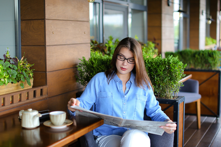 Young woman resting at restaurant with newspaper and cup of tea.の写真素材
