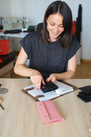female carefully preparing leather for making black purse. Young woman decided to start business and...