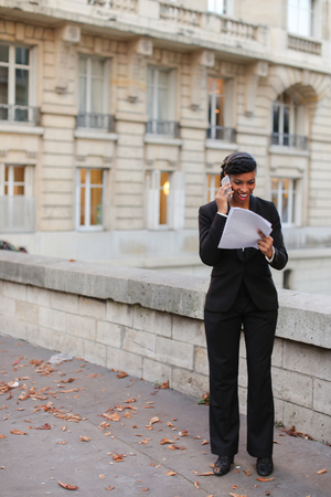 African American discussing work using silver smartphone and walking on bridge with papers in hands.の写真素材
