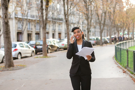 Young half Nigerian girl excited about date talking by smartphone with boyfriend and walking.の写真素材