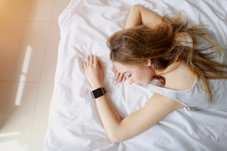 portrait of young woman with smartwatches on hand sleep in white bed. concept of monitor sleeping patterns on electronic watch, health check habbitsの写真素材