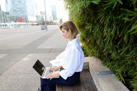 Female statistician working with color diagrams and laptop outdoors near green plant. Concept of working with theoretical or applied statistics. Young woman wears business clothes.の写真素材