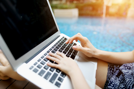 Family Fingers typing on the computer keyboard. Close up portrait of woman and little girl hands pressing buttons on laptop at sunny day swimming pool. concept of business freelance working, new technologiesの写真素材