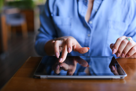 Young girl using tablet at restaurant and sitting on blue sofa. Beautiful girl wears in casual and has pony tail. Concept of wireless local area network at catering establishment and browsing.の写真素材
