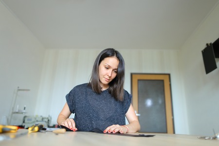 Female slicing leather using special knife, ruler and scissors, young lady recently got job in atelier.の写真素材