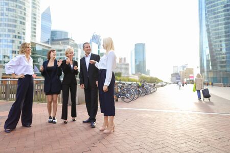 Beautiful businesswomen keeping blue document case talking with cheerful male boss outside. Concept of speaking with partners and joking about work. Pretty ladies dressed in white shirts smiling with man.の写真素材
