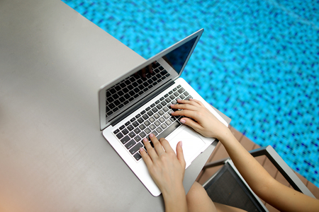 view from above Fingers typing on the computer keyboard. Close up portrait of woman hands pressing buttons on laptop at sunny day swimming pool. concept of business freelance working, new technologiesの写真素材