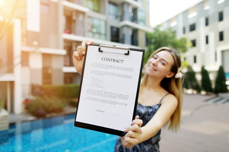 beautiful young girl extends contract, focus on document. concept of offices for delivery of housing, real estate real estate long-term or short-term lease. Front used with Open Font Licenseの写真素材
