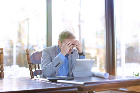 Management consultant talking with client by tablet using headset phones with microphone and sitting at cafe.の写真素材