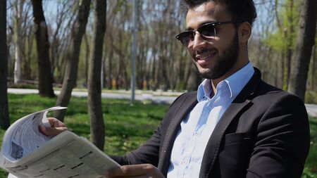Close-up photography, man reading newspaper and smiling with dimples on face. Guy has beard and short hair. Arab dressed in black jacket.の写真素材