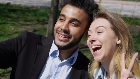 Siblings looking at phone s screen, man leaf photos. Lady has beautiful long hair and dressed in denim shirt, white T-shirt. Good looking man has beard, short hair and dimples on cheeks. Concept of traveling good camera modern technology.の写真素材