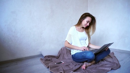 Charming young woman prints on gadgets keyboard and rewrites in social networks or watches video onlineの写真素材