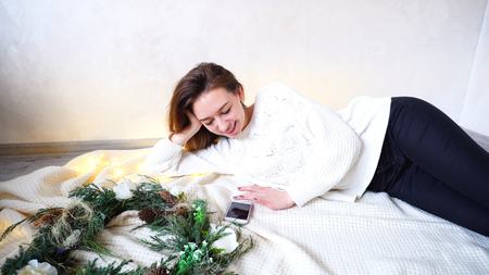 Beautiful girl drives fingers on touch screen of modern phone and rewrites in social networks or sends out congratulations to new year to friends. Woman smiles and laughs with beautiful broad smile.の写真素材