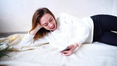 Beautiful Woman with smile on face answers and writes messages on mobile, looks at gadgets screen and sees joyful news, rejoices and rejoices.の写真素材