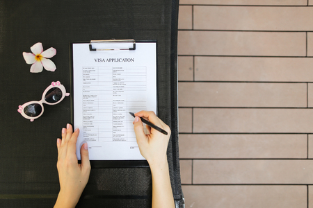flat lay of woman hands fill  application for business travel, sunlight portrait with sunglasses and tropical flower.の写真素材