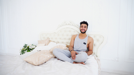 Charming Dark-Skinned and Muscular Guy Arab Sits on Bed With Knees Bent Legsの写真素材