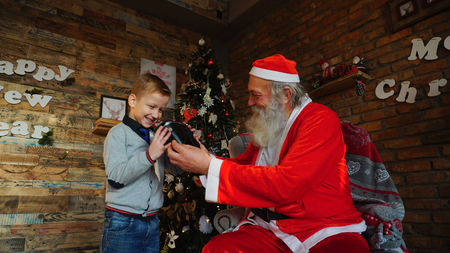 Child shakes box with gift trying to guess whats in middle. Boy neatly combed and dressed in gray sweater and shirt with tieの写真素材