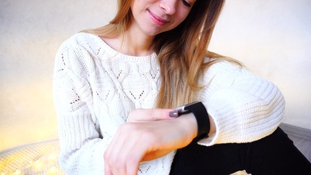 Good-looking Young Woman tunes and tests gadget that is worn on arm. Woman smiles and leads finger along small touch screen of modern electronic clock.の写真素材