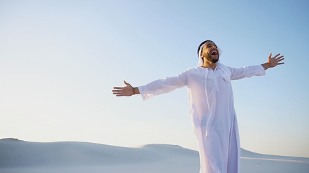 Stately young male Arab man in good mood conducts financial training of money, smiles and laughs joyfully launches money to windの写真素材
