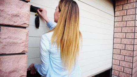 Female person opening white door with keys and showing place for car. Concept or renting house with big garage. Girl wears blue jeans shirt.の写真素材