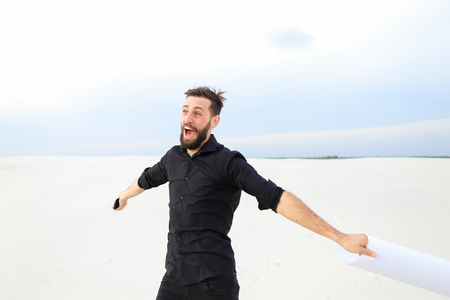 chemist pass quest from friends for birthday, fellow get poster with congratulations jumping for joy. Bearded guy has good mood walking running among sands. Concept of beautiful landscapes, innovative technologies or stylish outfits.の写真素材