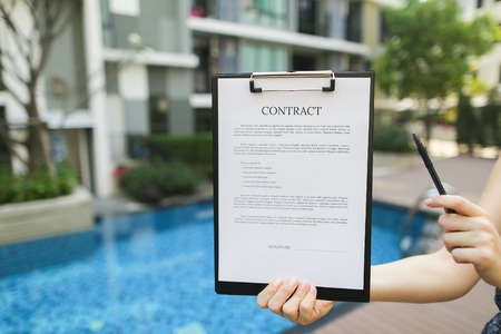woman is holding pen and contract, proposes to sign document against background of building with apartments. concept of signing papers, travel rental housing. Front used with Open Font Licenseの写真素材