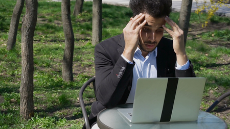 Man put arms on head and thinking about new building. Muslim sits by table and uses laptop. Professional has dark hair, beard and dressed in black jacket, blue shirt. Concept of modern technologies programs for worker on laptop and online projects.の写真素材