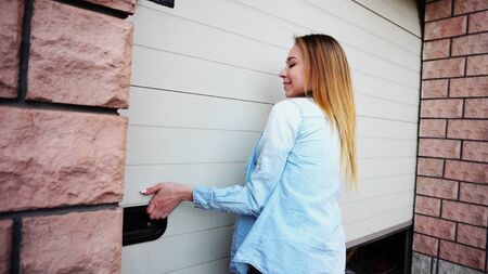 Female person opening white door with keys and showing place for car. Concept or renting house with big garage. Girl wears blue jeans shirt.の写真素材