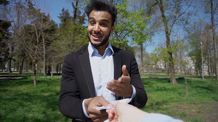 Attractive guy talking with woman and gets to use phone.Female handwith pink nail varnishclicks on screen. Smiling man has dimples on cheeks, beard and dark hair. Guy dressed in black jacket and blue shirt. Concept of internet selling and modern technologies good nail varnish.の写真素材