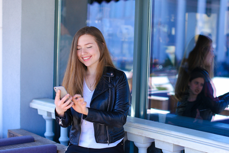 Gladden girl chatting by smartphone at street cafe. Concept of enjoying social networks.の写真素材