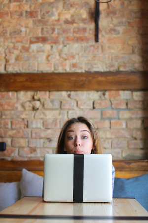 Student enjoying with laptop at cafe. Concept of making faces and modern gadgets.の写真素材
