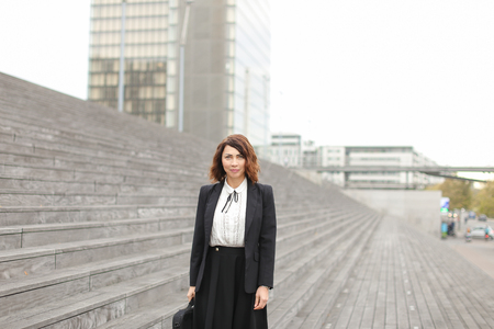 Successful businesswoman standing on stairs with bag and high buildings in background. Concept of profession and business, cityscape.の写真素材