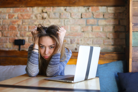 Upset girl sitting near laptop at cafe with brick wall background. Concept of modern technology,...