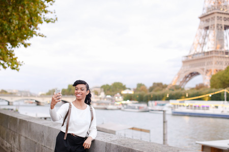 International black student walking near Eiffel Tower and Seine and making selfie by smartphone. Concept of education and tourism in Paris.の写真素材