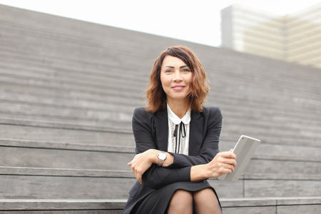 Caucasian secretary sitting on stairs with tablet. Concept of working in open ait and modern technology.の写真素材