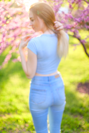 Female person wearing jeans standing in sun rays with blooming trees and green grass background.の写真素材