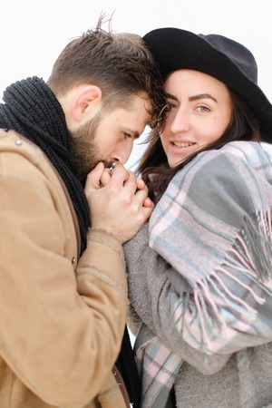 Portrait of caucasian man with beard holding woman hand in white background, wearing coat with scarf. Concept of couple seasonal winter photo session and romantic feelings.の写真素材