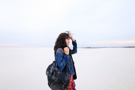 Stylish female person wearing jeans and bag standing in white winter background. Concept of fashionable look and seasonal photo session.の写真素材