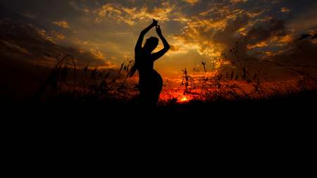 Female person black silhouette doing asanas in steppe, sunset background. Concept of yoga practise and relaxing.の写真素材