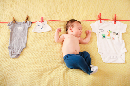 Little nice baby hanging with clothes on rope. Concept of funny photo session for babies.の写真素材