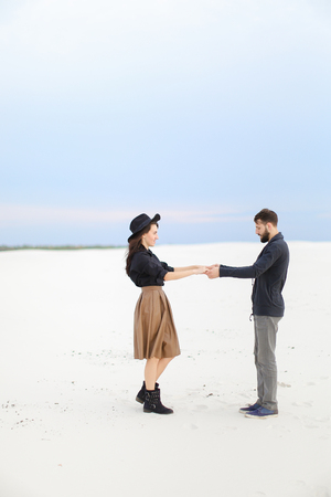 Young european woman wearing skirt nad hat holding hands of handsome man on snow in white background. Concept of feeling and romantic photo session.の写真素材