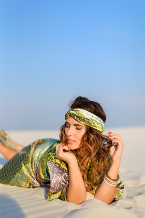 Young girl wearing green beach robe lying on white sand. Concept of sunbathe and photo session in desert.の写真素材