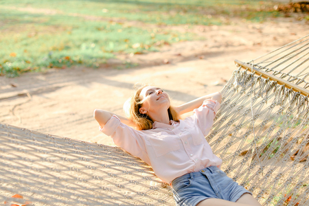 Young woman lying on white wicker hammock with sand in background. Concept of having leisure time on beach and summer vacations.の写真素材