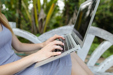 Female caucasian person using laptop, palms in background. Concept of exotic summer vacations and...