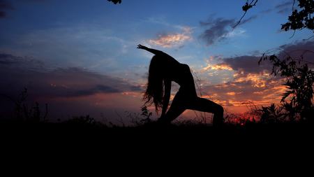 Woman shadow doing yoga, female silhouette in evening sky background. Concept of asanas and relaxing before night.の写真素材