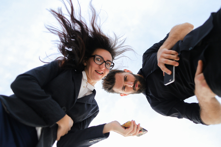 Photo from below, young businesswoman and businessman keeping smartphone in white monophonic background. Concept of modern technology and business.の写真素材