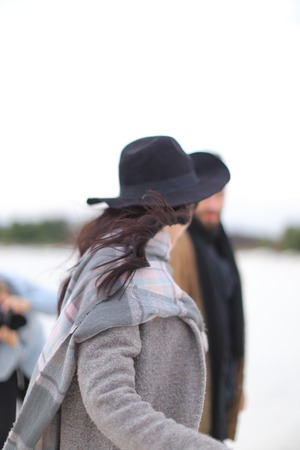 Young happy woman wearing hat and grey coat with scarf standing in white winter background. Concept of seasonal inspiration photo session.の写真素材