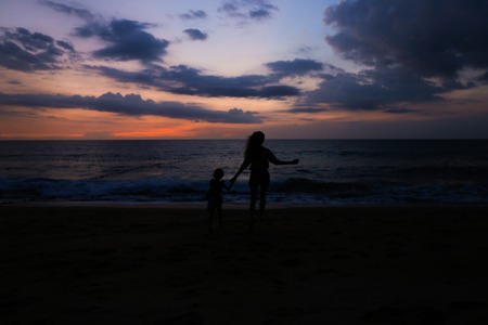 Black silhouette of mother running with little girl on sea shore in sunrise background. Concept of calm evening and happiness, summer vacations.の写真素材