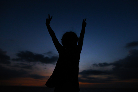 Silhouette of little female child with outstretched hands in sunset sky background. Concept of calm evening and freedom in childhood.の写真素材
